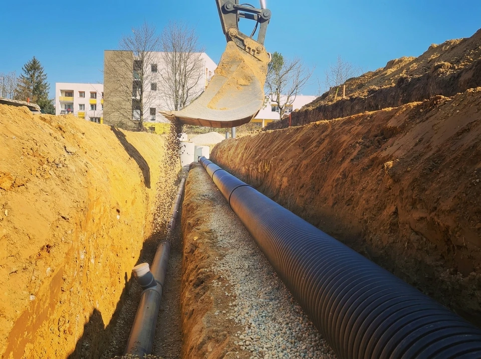 Chantier de travaux publics en extérieur avec tranchée ouverte et canalisations grises installées dans coffrages béton préfabriqués
